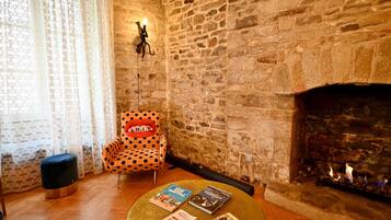 Quarto aconchegante com parede de pedra, lareira, cadeira com estampa de bolinhas e mesa redonda com livros.