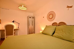 A bedroom with a bed, a desk with a lamp, a wardrobe, and decorative wall art. - Historic Center Apartment – Fireplace, Stone Walls & Jungle Decor (Vannes)