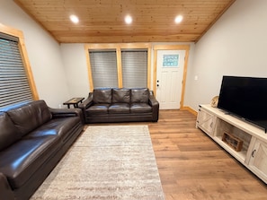 Ein Wohnzimmer mit einem braunen Ledersofa, einem Fernseher auf einer Holzeinrichtung und einer Tür mit Glasfenster.