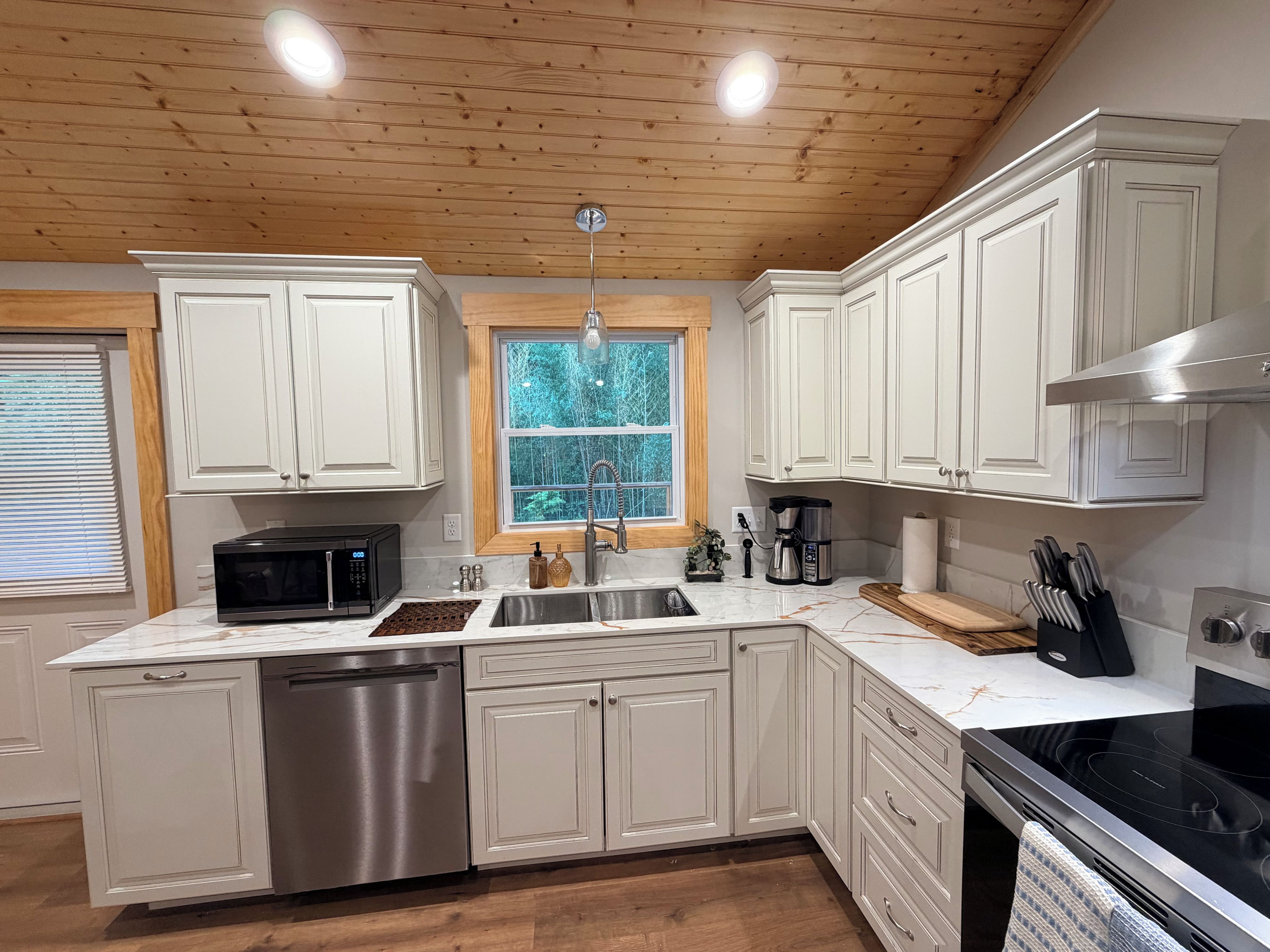 A modern kitchen with white cabinetry, a stainless steel dishwasher, a black microwave, a sink, and a black stove.
