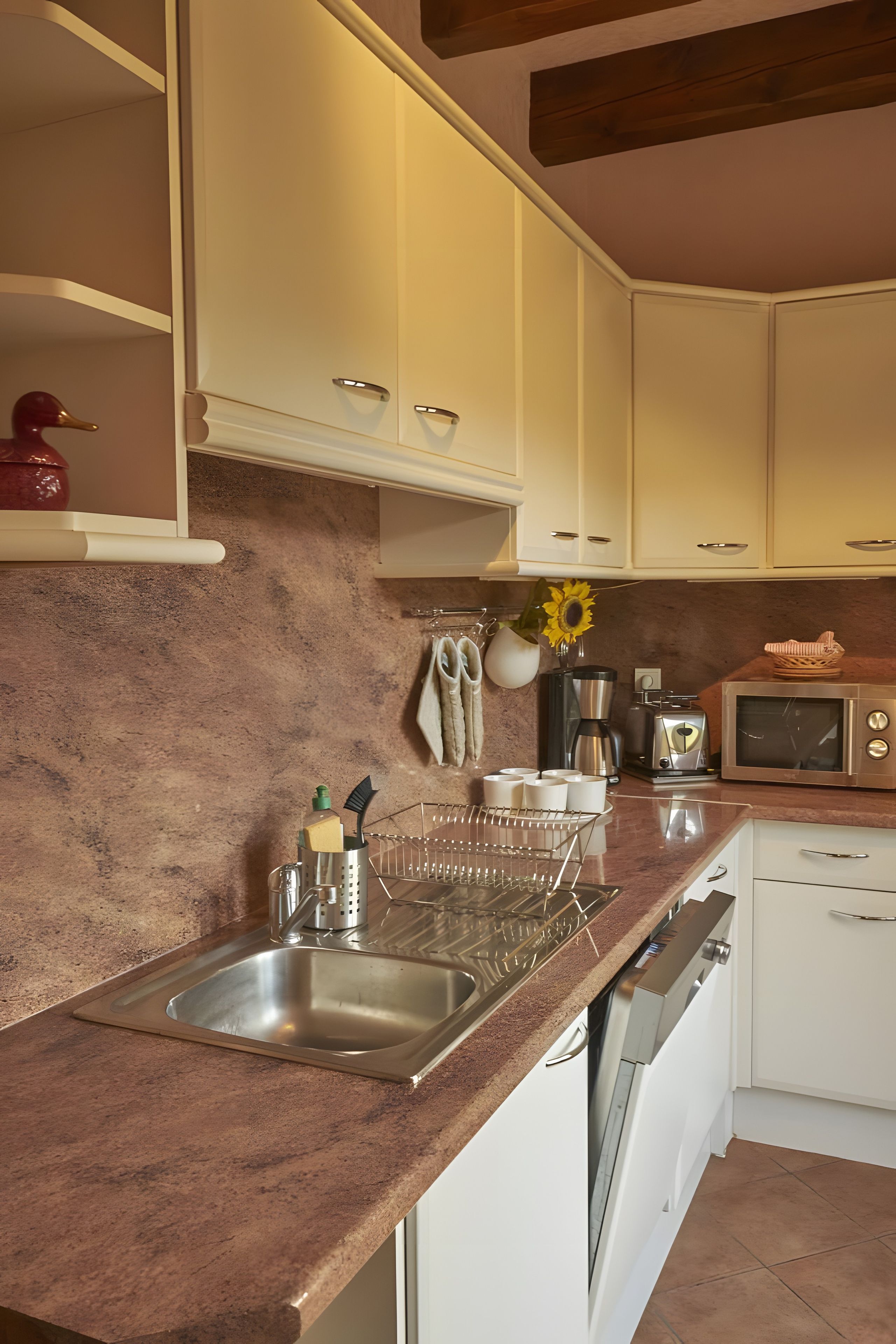 Een keuken met witte kasten, een roestvrijstalen spoelbak, een magnetron en een koffiezetapparaat.