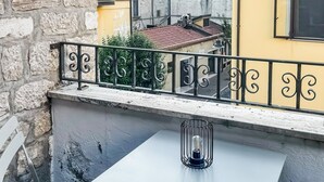 Varanda com mesa e cadeiras brancas, grade de metal e vista para edifícios coloridos.