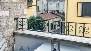 Un balcon avec une table et des chaises blanches, une rambarde en métal et une vue sur des bâtiments aux couleurs vives.