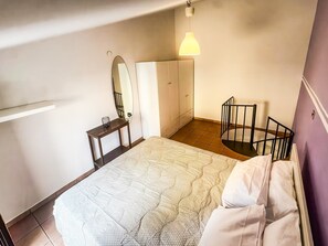 Un dormitori amb un llit, una petita taula de nit, un mirall i una cadira.