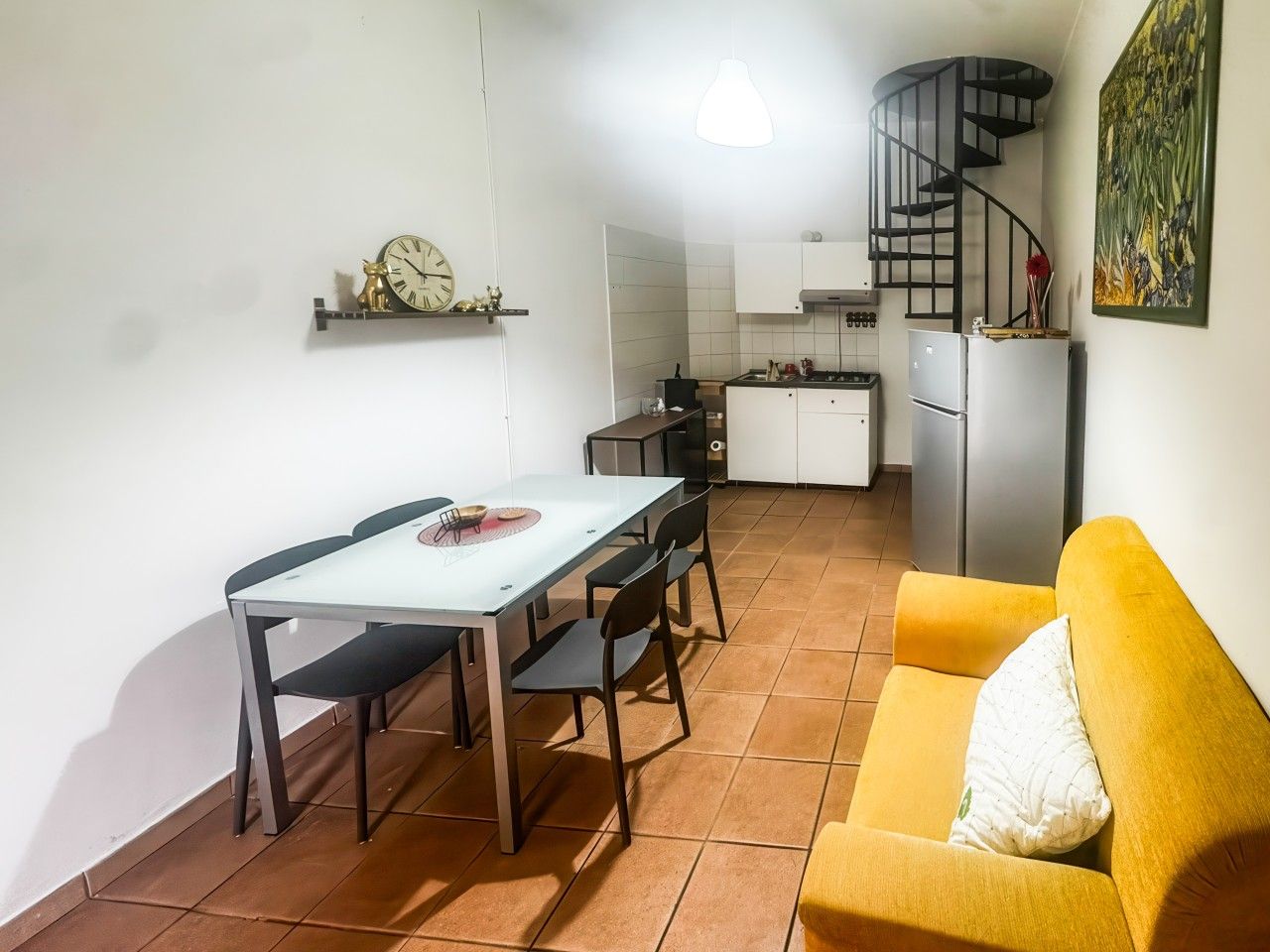 Ett kompakt bostadsutrymme med matplats, kök och en trappa.