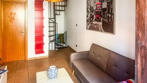 Uma sala de estar com sofá, mesa de centro, escada com degraus vermelhos e luminária na parede.