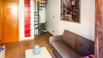 Un salon avec un canapé, une table basse, un escalier aux marches rouges et une lampe fixée au mur.