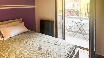 A bedroom with a bed, a window, and a view of a balcony.