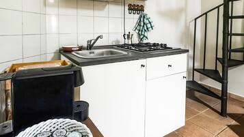 Una cucina con mobili bianchi, un fornello a gas, un lavello e una scala a chiocciola nera.