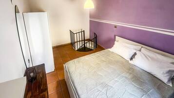 A bedroom with a bed, a small table, a chair, a wardrobe, and a hanging light fixture.
