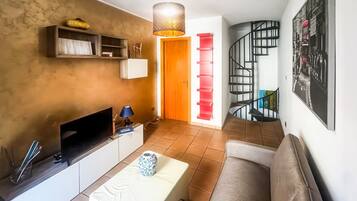 Un salon moderne doté d’un téléviseur à écran plat, d’un canapé blanc, d’une table basse et d’un escalier menant à un niveau supérieur.