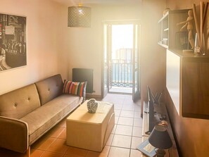 A living room with a sofa, a coffee table, a lamp, and a television. There is a door leading to a balcony. - Le Dimore - Potenza: Three-Level Apartment in the Historic Center of Potenza (Potenza)