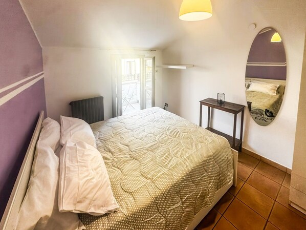 A bedroom with a bed, a bedside table, a lamp, a window, and a door.