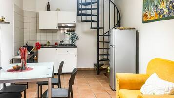 Un espace de vie compact comprenant une cuisine, un coin repas et un canapé jaune.