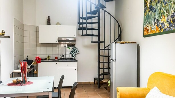 Espaço compacto com cozinha, área de refeições e sofá amarelo.