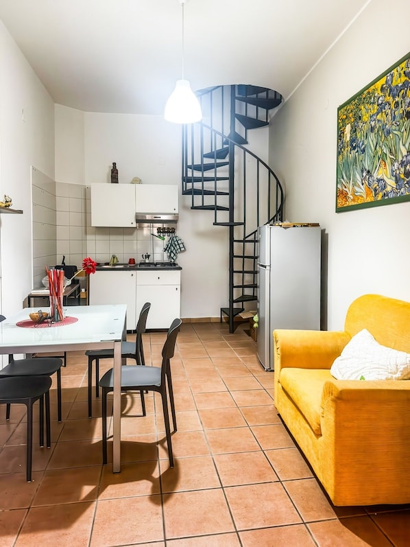 Un ambiente compatto con angolo cottura, zona pranzo e un divano giallo.