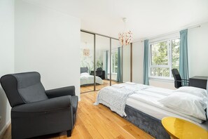 Un dormitorio moderno con una cama, una silla, un escritorio y un espejo grande.
