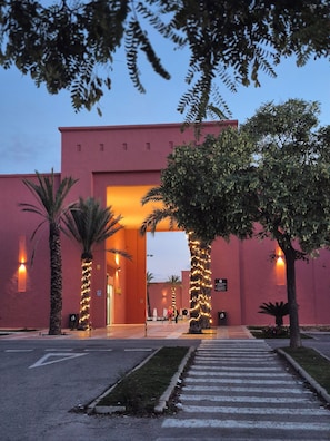 Ein Gebäude mit roter Fassade, Palmen und einem Fußweg zum Eingang.