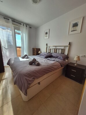 A bedroom with a bed, a nightstand, a lamp, and two wall-mounted pictures. - Home away from Home in the Sun (MC)