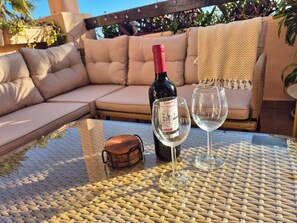 A wicker table with a wine bottle and two glasses, a cushioned outdoor sofa, and a wooden pergola. - Home away from Home in the Sun (MC)