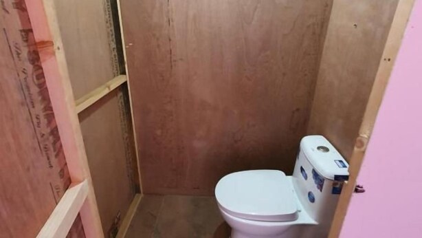 Ein kleines Badezimmer mit Toilette in Weiß, einer Duschkabine und einer rosa Wand.