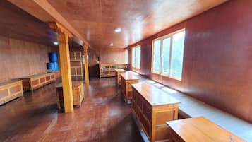Una habitación con bancos y mesas de madera, ventanas amplias y techo de madera.