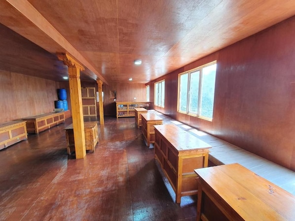 A room with wooden benches and tables, large windows, and a wooden ceiling.