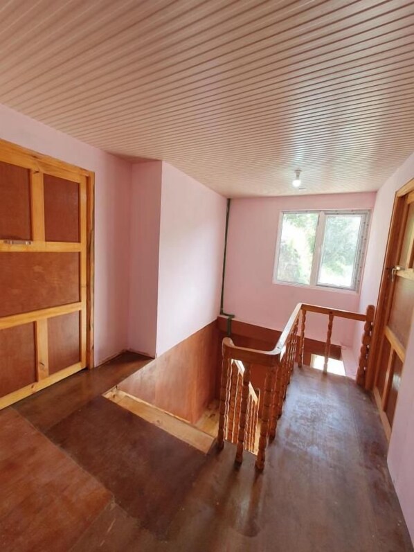 Una habitación con techo inclinado, una silla de madera, un ventanal y una puerta.