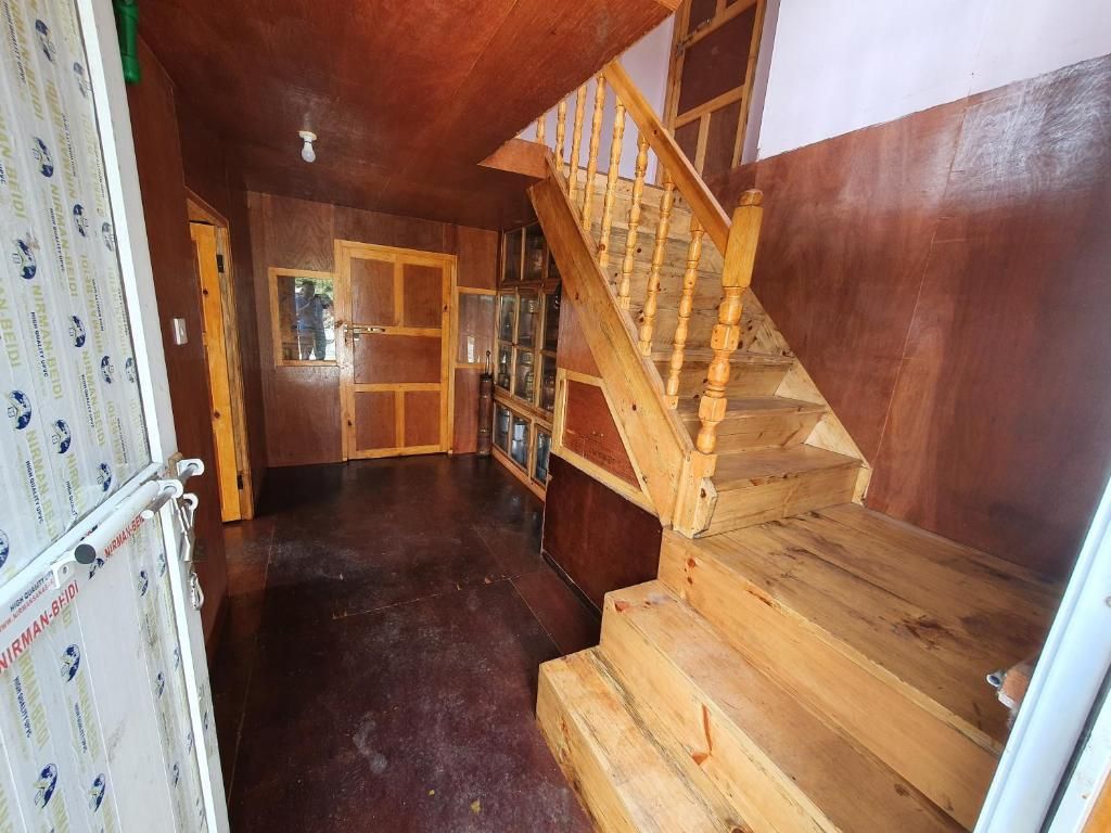 Una escalera de madera que conduce a un segundo piso, un armario con puerta de vidrio y un refrigerador con forro estampado.