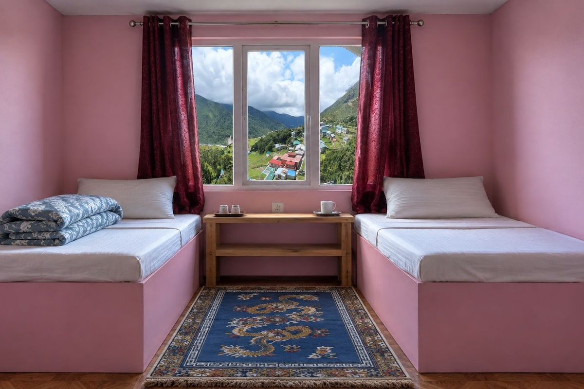 A room with two beds, a small table, and a view of a mountainous landscape.