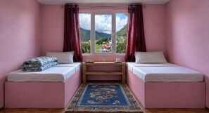 Een kamer met twee bedden, een tafeltje en uitzicht op een bergachtig landschap.