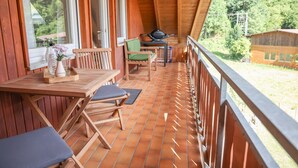 A wooden deck with a table and chairs, a grill, and a view of the surrounding forest. - Apartment 'Ferienwohnung Schätzle' (Fischerbach)