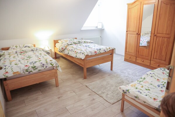A bedroom with two wooden beds, a wooden wardrobe, and a mirror.