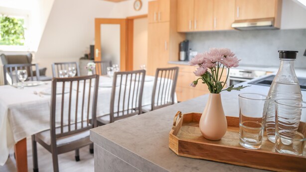 A modern kitchen with wooden cabinets, a dining area with chairs, and a vase with flowers on the counter. - Apartment 'Ferienwohnung Schätzle' (Fischerbach)