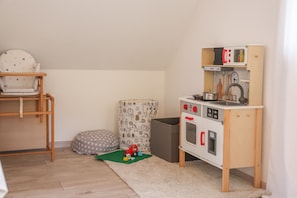 A child's playroom with a wooden chair, a play kitchen, and a soft rug.