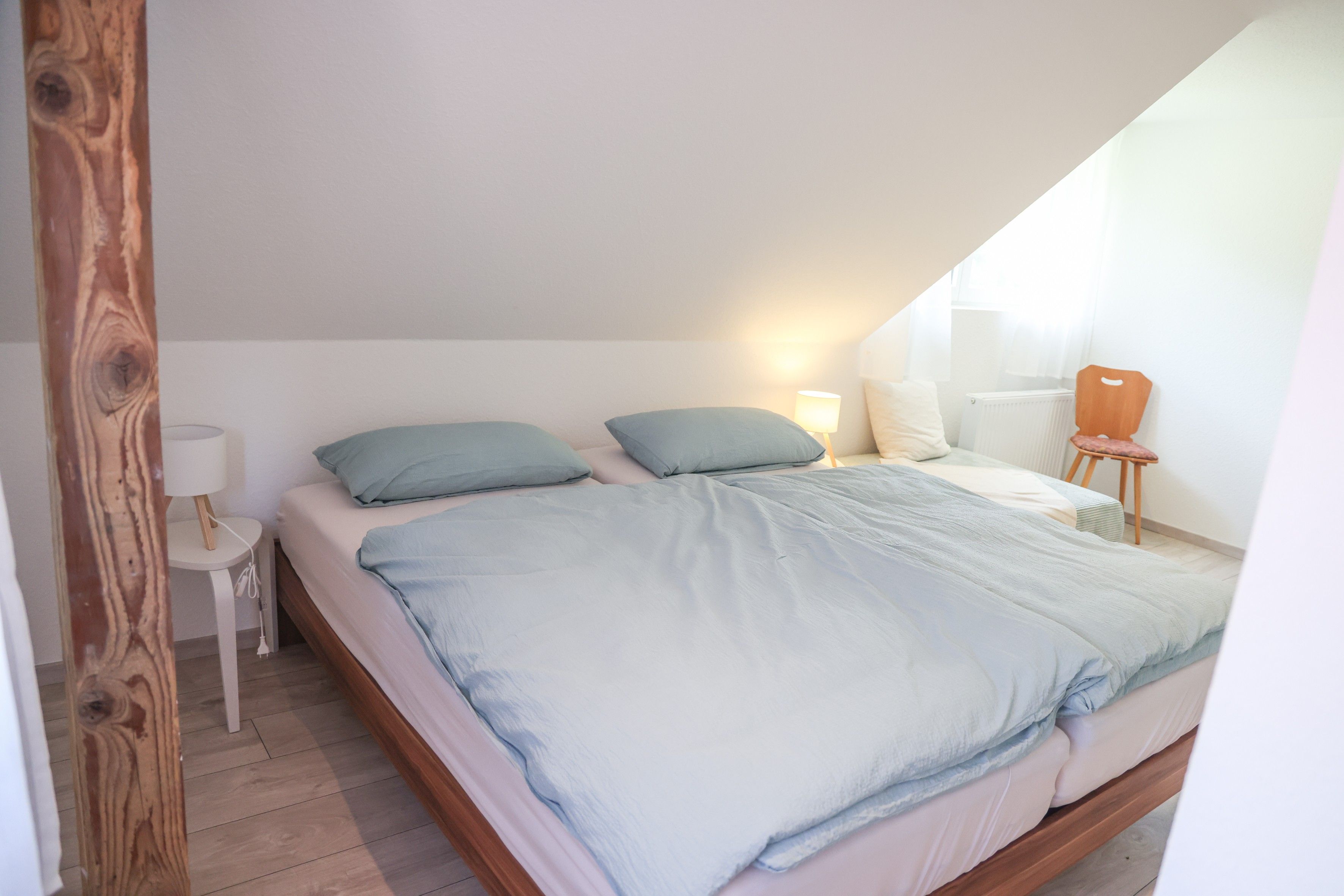 Een slaapkamer met een bed, kussens, een nachtkastje, een lamp en een radiator.