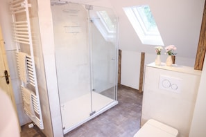 Un baño moderno con cabina de ducha de vidrio, perchero y tragaluz.