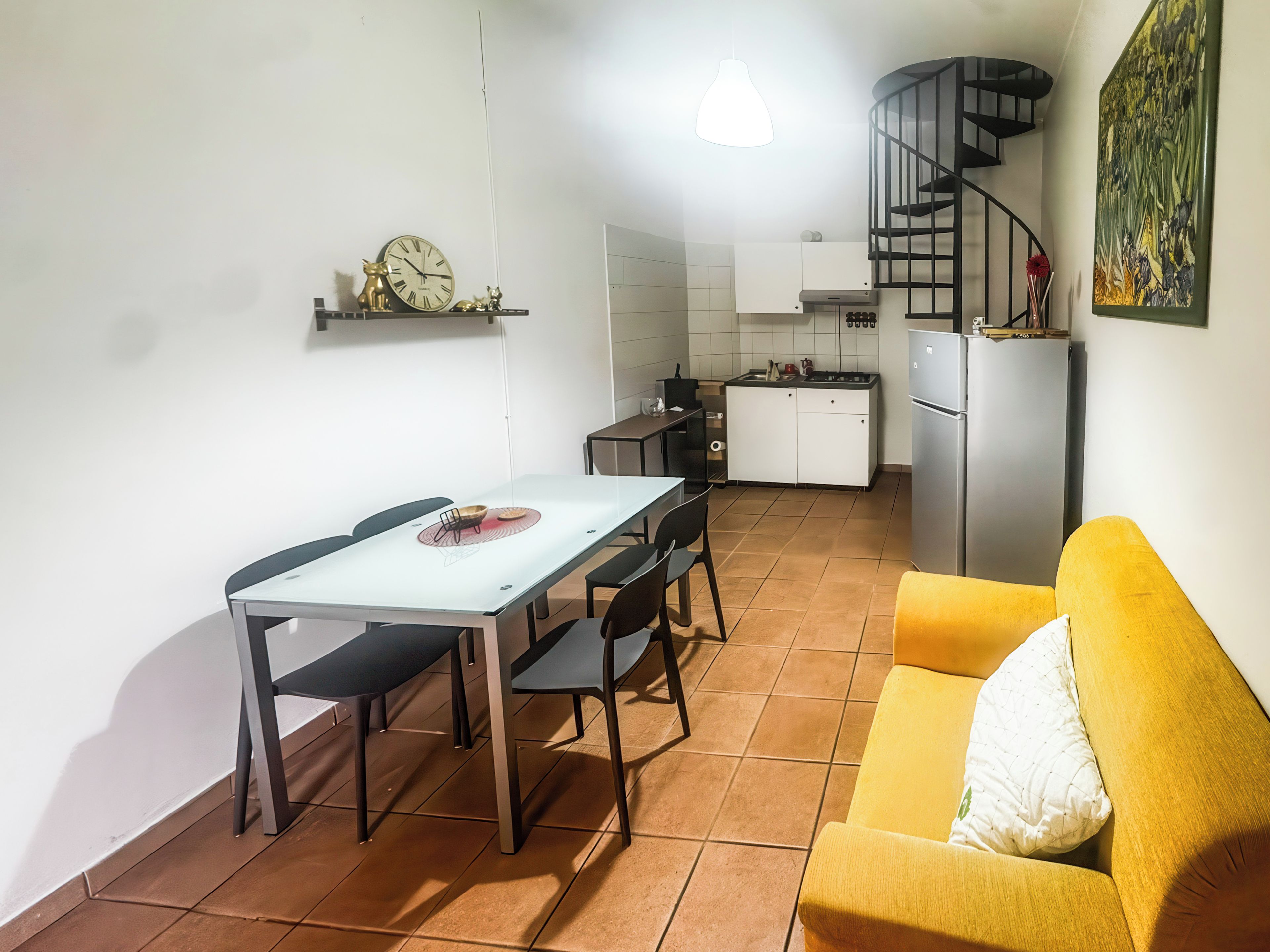 Un espacio habitable compacto con mesa de comedor, sillas, sofá, zona de cocina y una escalera de caracol.