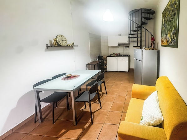 A compact living space with a dining table, chairs, a sofa, a kitchen area, and a spiral staircase. - Le Dimore - Potenza. (Potenza)