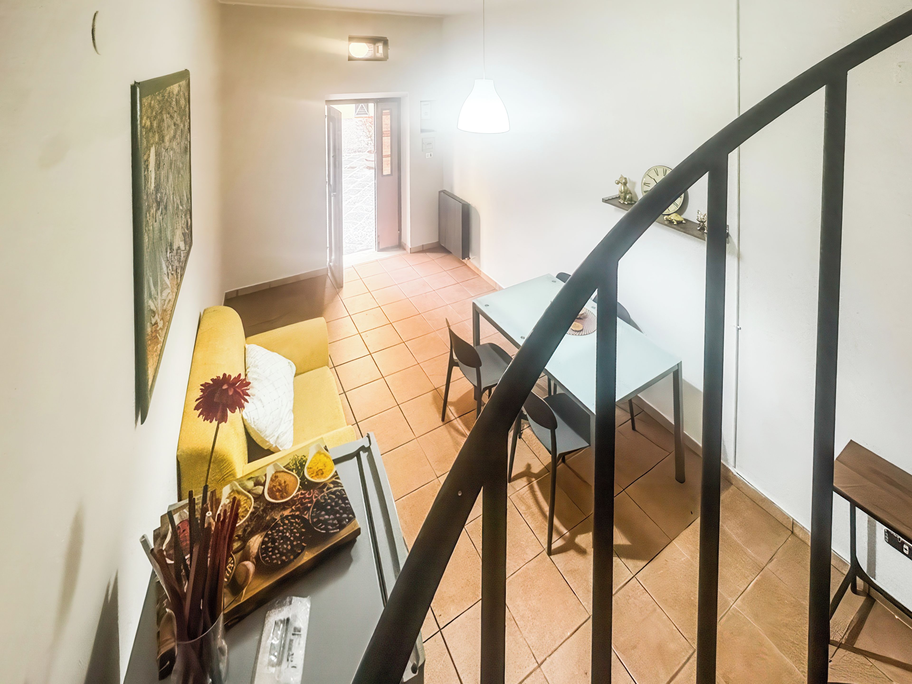 Una escalera conduce a un comedor con una mesa, sillas, un sofá amarillo y un cuadro en la pared.