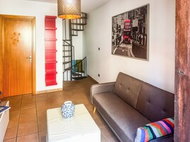 Un soggiorno con divano, tavolino, una scala rossa, una scala a chiocciola e un quadro appeso al muro.