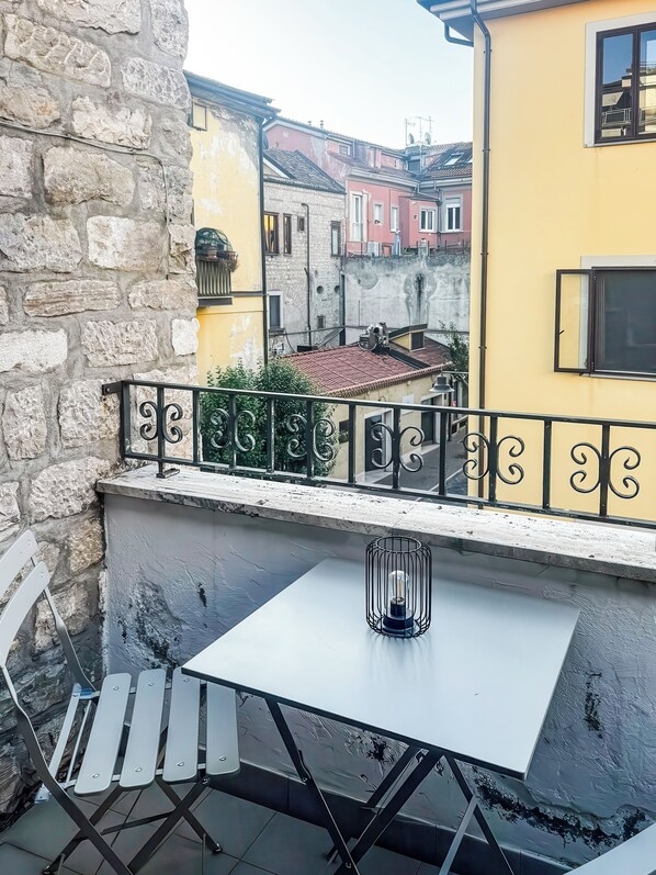 A balcony with a white table and chairs, a metal railing, and a view of colorful buildings in the background. - Le Dimore - Potenza. (Potenza)