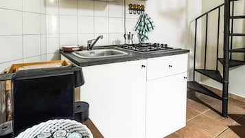Una cocina con armarios blancos, una estufa a gas, un lavamanos y una escalera en espiral negra.