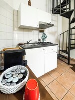 Una cucina con mobili bianchi, un piano cottura a gas, un lavello e una scala a chiocciola nera.