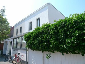 Ein weißes Gebäude mit weißem Zaun und einer grünen Hecke. Fahrräder sind davor abgestellt.