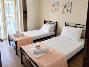 A hotel room with two single beds, each with a white pillow and a rolled towel. There are two wall-mounted paintings of flowers. - Zografou Two Bedroom Apartment Near Central Athens (Zografou)