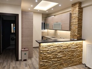 A modern kitchen with a stone accent wall, recessed ceiling lights, and a built-in sink. - Zografou Two Bedroom Apartment Near Central Athens (Zografou)