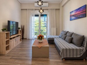 A modern living room with a flat-screen TV, a sofa, a coffee table with a vase of flowers, and a balcony with a view. - Zografou Two Bedroom Apartment Near Central Athens (Zografou)
