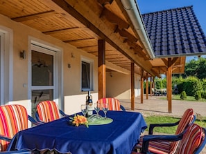Eine Terrassengruppe im Freien mit Tisch für zwei Personen, umgeben von gestreiften Stühlen, unter einer Holz-Pergola mit Ziegeldach.