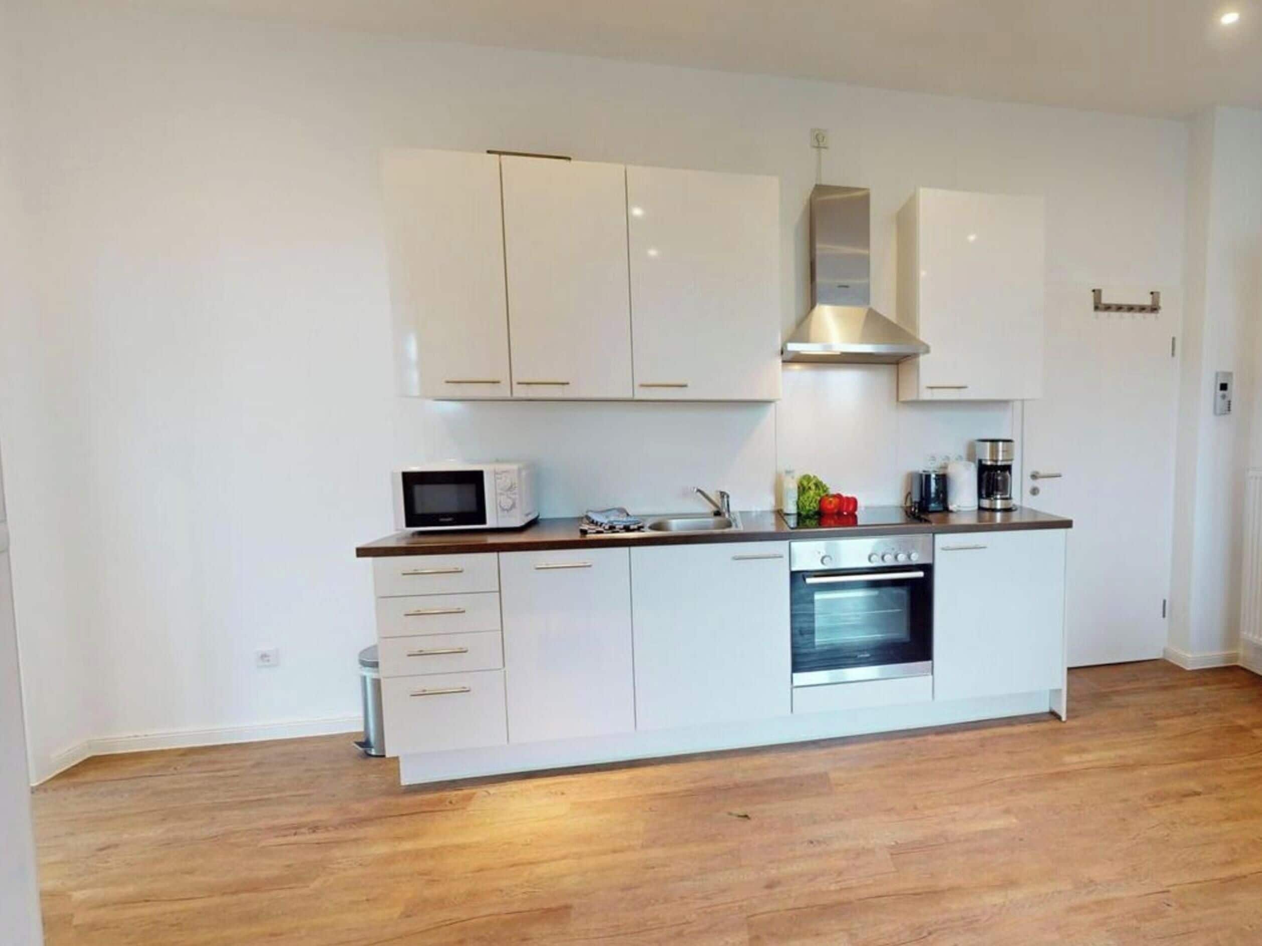 A modern kitchen with white cabinets, a microwave, a stove, and a coffee maker.